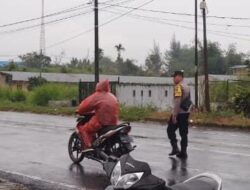 Bhabinkamtibmas Polsek Raya Tetap Bertugas Atur Lalu Lintas di Simpang Sekolah Meski Diguyur Hujan